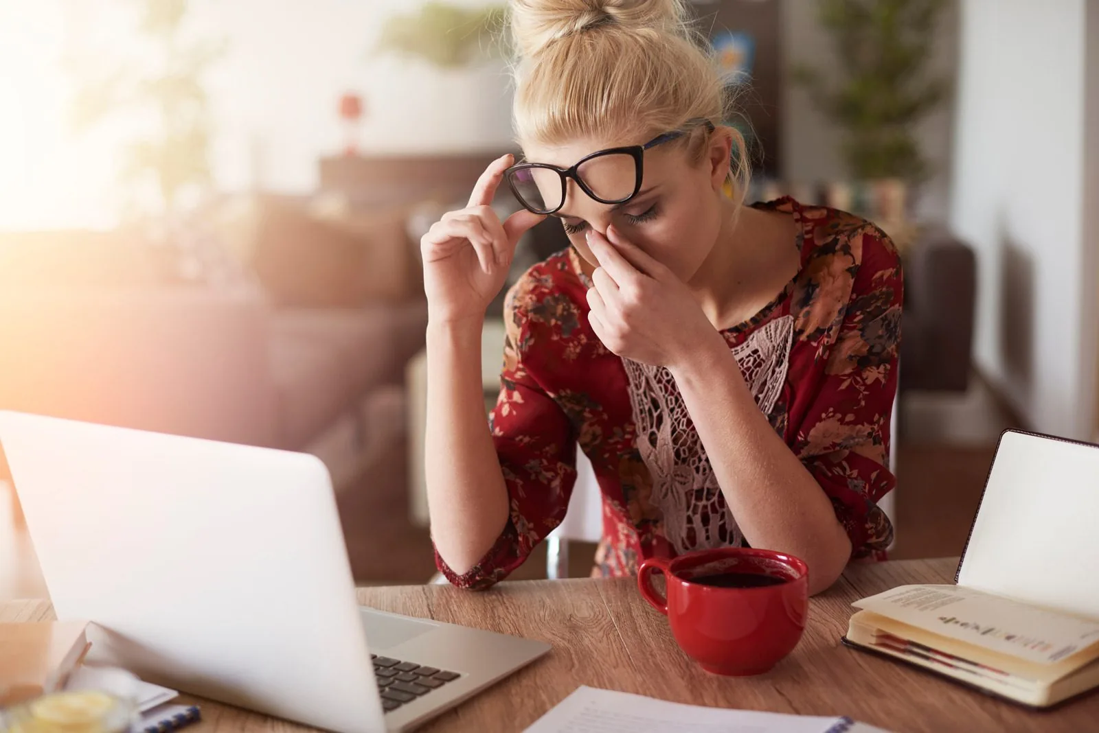 Woman with glasses pushed up rubbing her eyes at a laptop